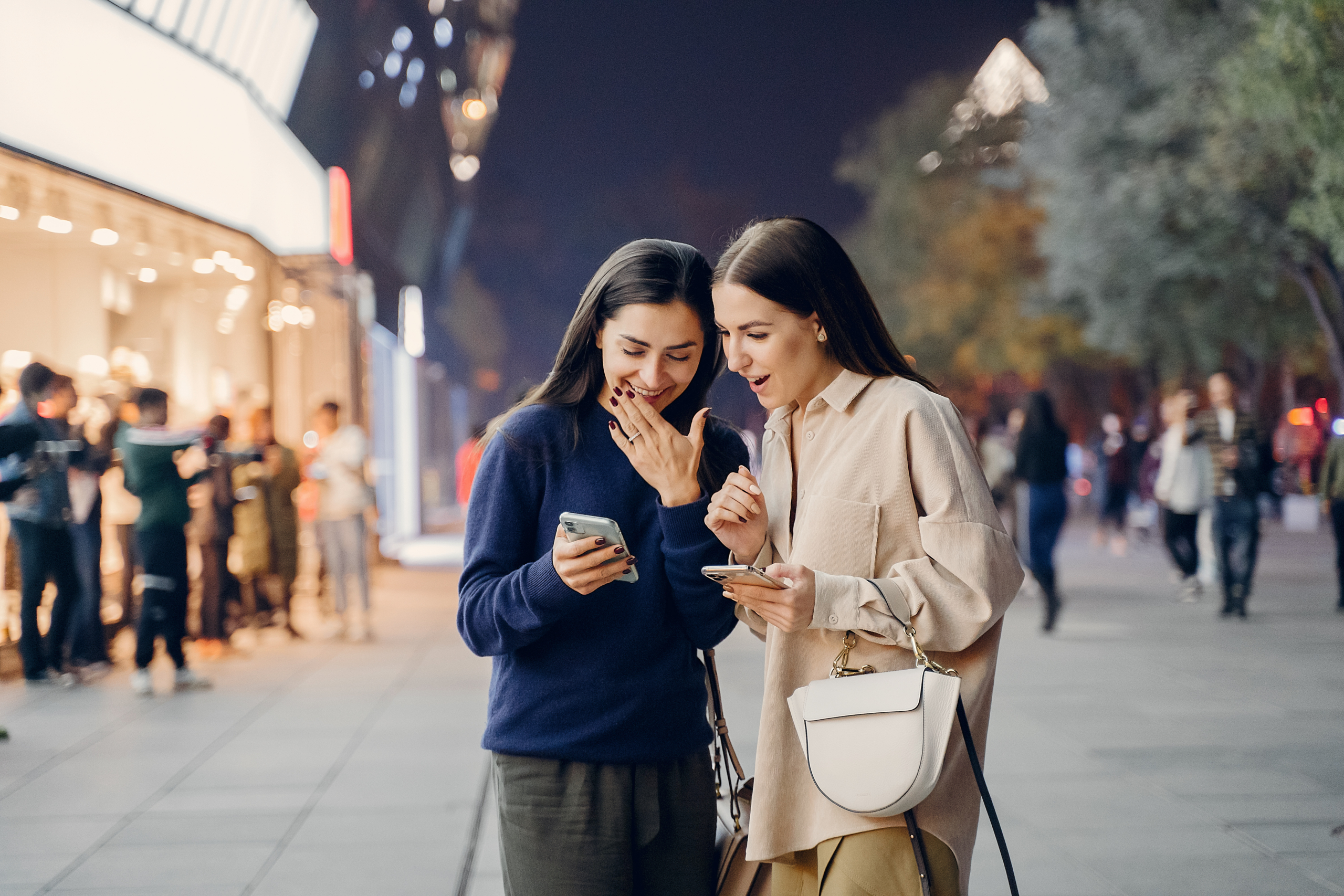 two girlfriends using their cellphone while exploring a new city at night
